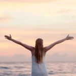 rear view of woman with arms raised at beach during sunset 320007 scaled e1592662793814